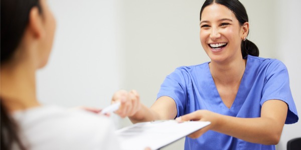 A smiling medical assistant passing paperwork over to a patient.