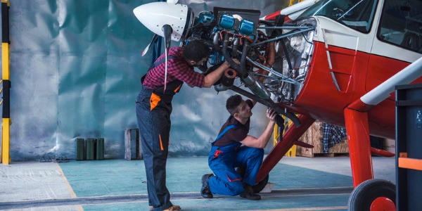 Two aircraft mechanics repairing and performing scheduled maintenance on an airplane.