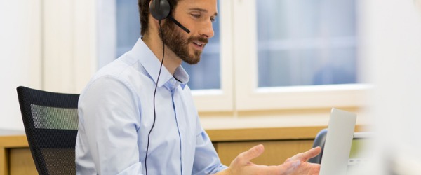 An IT support specialist sitting at a desk, looking at his computer, and providing online technical support to a customer.